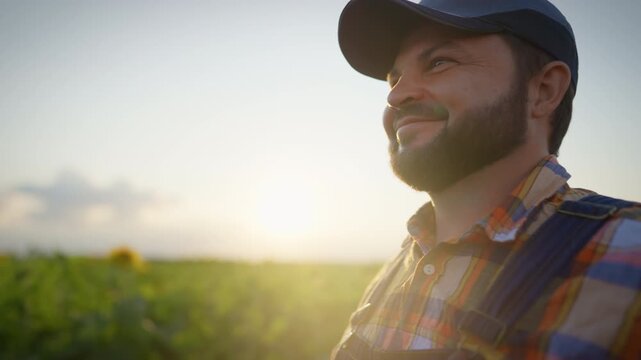 Happy farm worker smiling when viewing beautiful green field, rural scenery. Portrait of bearded farmer and agronomist admiring beauty of nature in agricultural region, grow plants for food industry