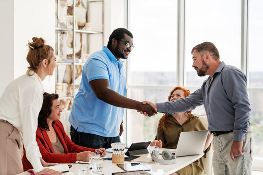 Diverse business team watches two colleagues shake hands