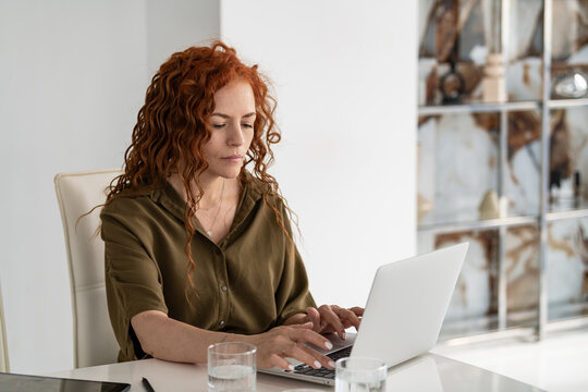 Focused woman with red hair typing on a laptop