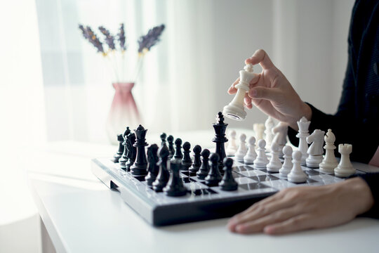 Hand of businesswoman moving white king chess piece on chessboard for business strategy leadership competition and management success concept