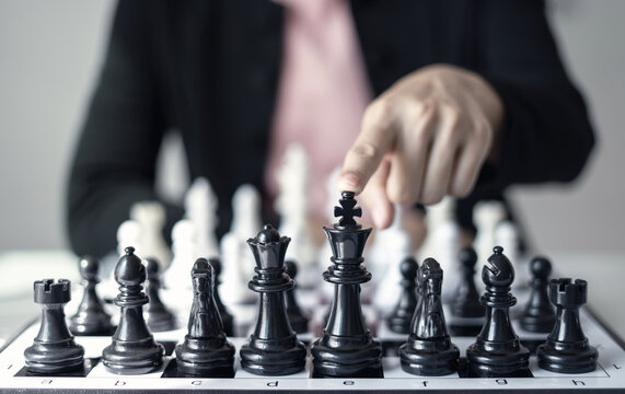Hand of businesswoman pointing black king chess piece on chessboard for business strategy leadership competition planning and management success concept