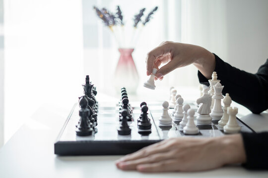 Hand of businesswoman moving white king chess piece on chessboard for business strategy leadership competition and management success concept