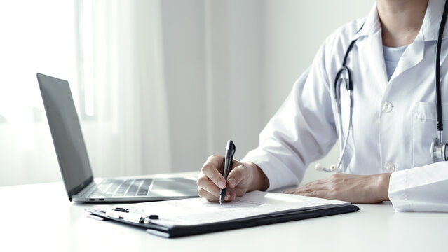 Doctor holding laboratory report document and pen to analyze medical patient health results near laptop on desk in hospital clinic office space