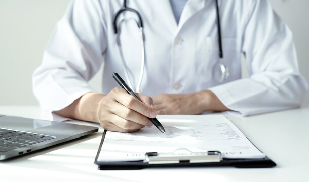 Doctor holding laboratory report document and pen to analyze medical patient health results near laptop on desk in hospital clinic office space