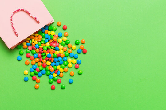 shopping paper gift bag in corner full of assorted traditional candies falling out on colored background with copy space. Happy Holidays sale concept