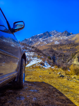 Dark Car Parked on Mountain Path with Snowy Peaks