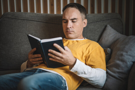 Thoughtful man reading a book with focused attention at home, enjoying a quiet moment.