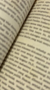 Vertical close-up video scrolling through open book pages with blurred text and shallow depth of field.