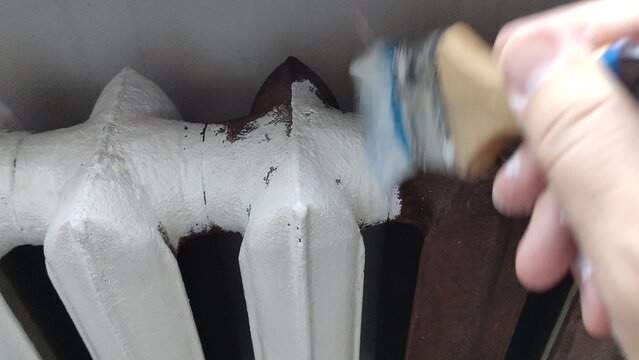 Person holding a paint brush and painting a cast iron radiator white, first person view video