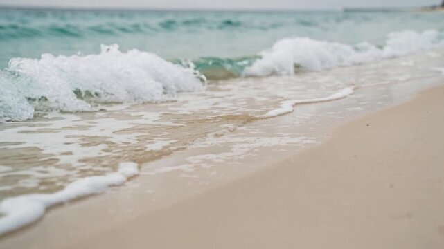 Calm ocean waves gently washing onto a sandy beach shore with soft blue water and white foam