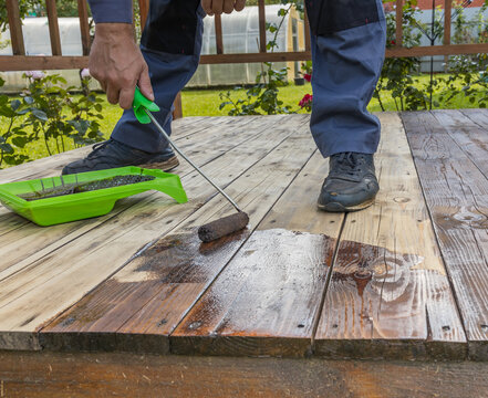 Close-up of someone staining wooden deck with brush