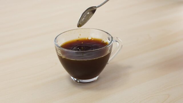 Stirring Black Coffee in a Clear Glass Mug with a Spoon