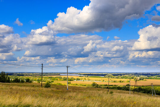 Sunlit rural plain with dramatic clouds, power lines, and distant horizon