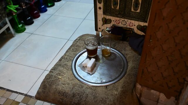 Marrakech, morocco. August 8, 2026. Traditional moroccan mint tea with sugar cubes served on a silver tray in a typical marrakech shop. Hookahs are visible in the background