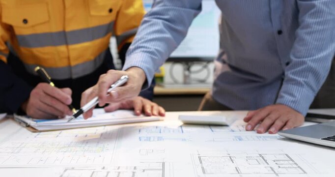 Engineers reviewing technical drawings and plans at a desk with a laptop and computer screen in a modern office.