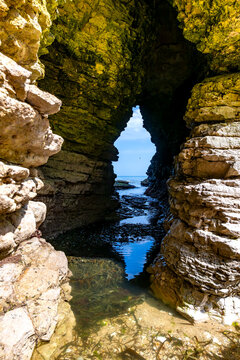 View through a natural sea cave at Flamborough Head on the Yorkshire coast, England. Eroded limestone cliffs frame the blue North Sea at low tide.