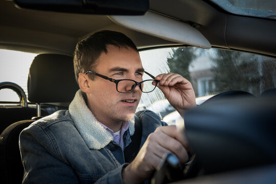 Male driver adjusting his glasses and looking ahead with a focused expression while driving. Correcting vision, paying attention to the road, and safe driving habits.
