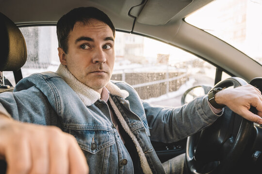 A man looks from behind the wheel of the car to the back of the car in astonishment. view on the side.