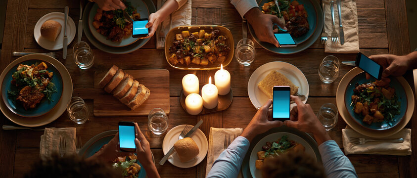 Friends and family share a candlelit dinner while scrolling phones perfect for campaigns on digital distraction, social dining, modern connection, or restaurant app advertising.