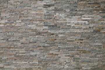 Natural stone wall made of quartzite strips with glittering effect. Colors are a mix of brown, gray and beige. Background and texture, full frame.