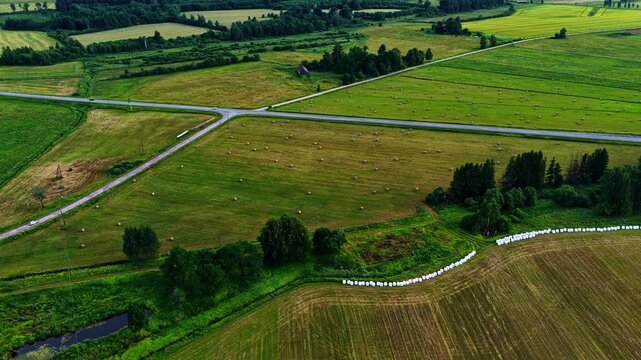 Green cultivated fields with hay bales and an asphalt road crossing the rural landscape