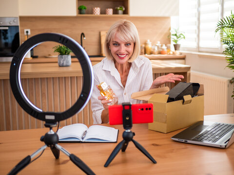 Female influencer filming an enthusiastic product unboxing video from her home content studio.