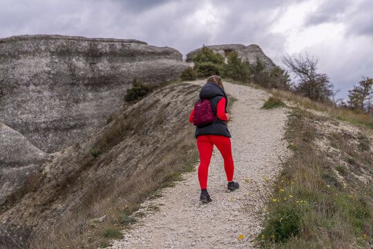 Active woman hiking rocky mountain trail wearing red leggings and black vest under cloudy sky