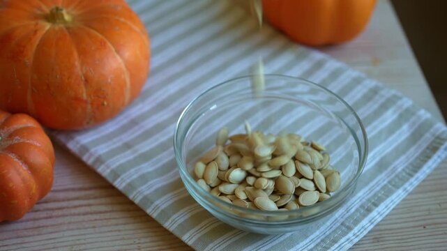 Raw dried pumpkin seeds in glass bowl close up with organic pumpkins on background. Healthy autumn snack.