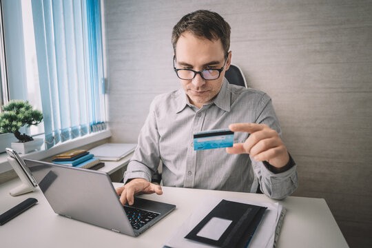 Businessman entering bank card data into laptop, financial transaction at desk.