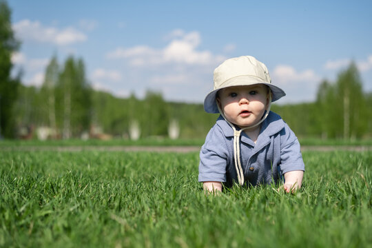 An adorable baby crawls on the green grass outdoors. A little boy is barefoot in the park.