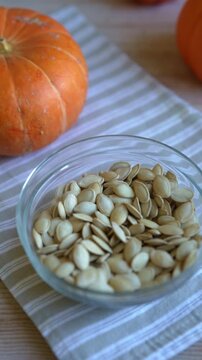 Raw dried pumpkin seeds in glass bowl close up with organic pumpkins on background. Healthy autumn snack.