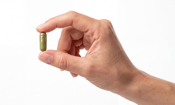 Hand holding a green capsule between fingers on a white background. Concept of supplements, medication, vitamins, nutrition, health and wellness.