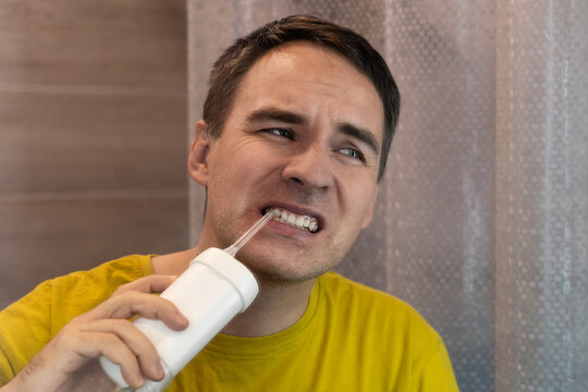 Man wincing in pain while using a water flosser on sensitive gums. Tooth pain, gum sensitivity, and uncomfortable oral care.