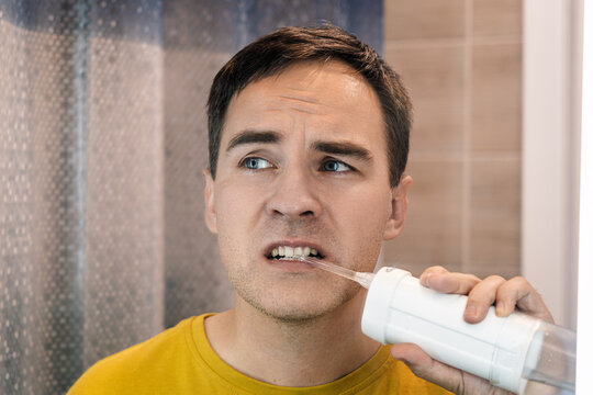 Young man using a water flosser for oral hygiene in bathroom, cleaning teeth with an irrigator while maintaining healthy dental care routine at home.