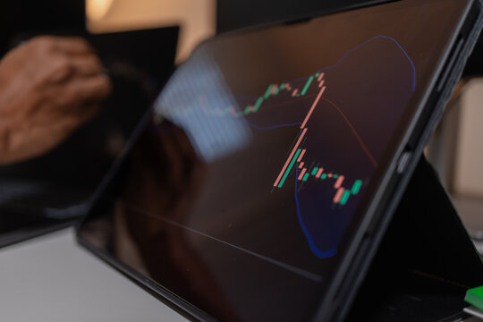 Professional trader analyzing stock market charts across multiple screens using laptop and tablet to monitor price movements, technical indicators and investment strategies in modern trading workspace