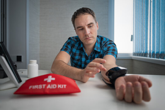 Man measuring his blood pressure at a table with a first aid kit nearby. Hypertension, hypotension, and cardiovascular health monitoring.
