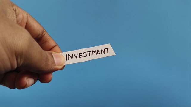 Hand holding white paper strip with investment return word or text written on it cut off using scissor. Symbolizing bad investment, business failure, money loss, market volatility and bankruptcy.
