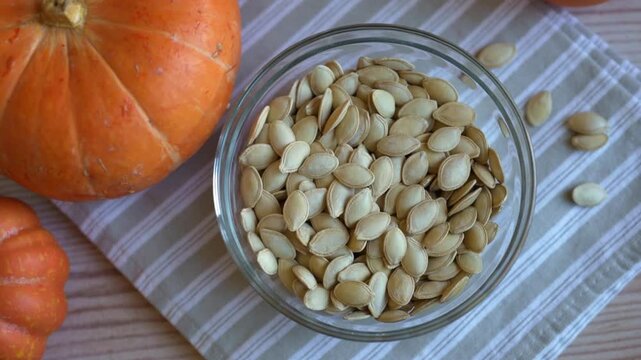 Raw dried pumpkin seeds in glass bowl close up with organic pumpkins on background.