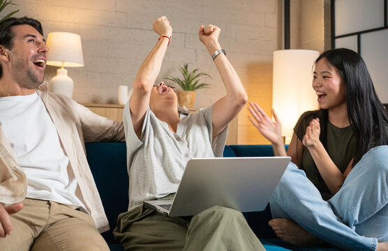 Group of friends cheering and laughing at home while watching content on a laptop