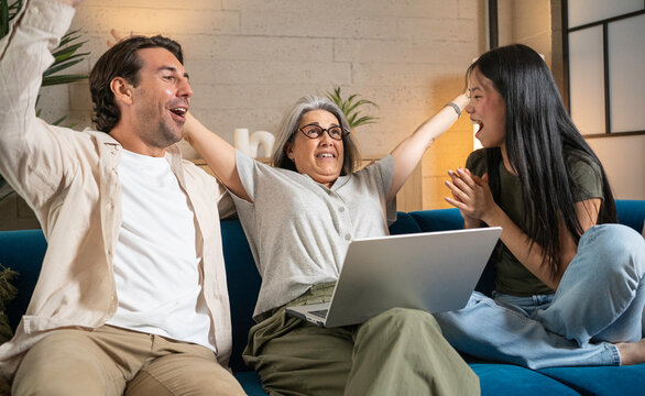 Happy multi-generational family cheering, celebrating victory with a laptop on the couch