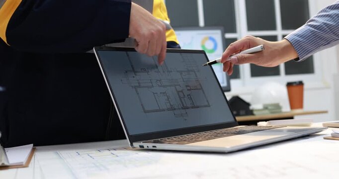Architects reviewing a building floor plan on a laptop, pointing at digital drawings during an office design meeting.