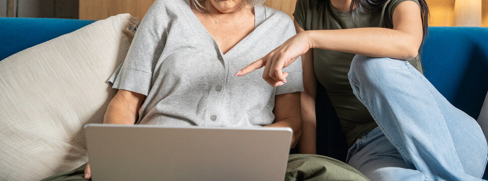 Woman assisting older female parent learning laptop skills on sofa