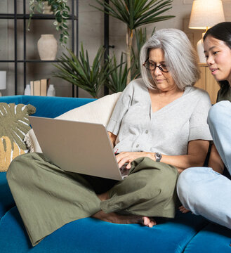 Senior woman and young woman collaborating on a laptop at home, bridging generations with technology