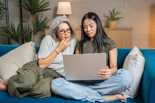 Two women using a laptop together on a sofa, sharing a digital experience