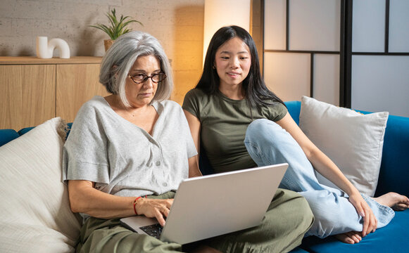 Adult daughter showing her senior mother how to use a laptop on the sofa at home