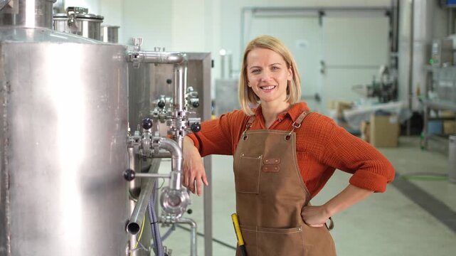 Confident female brewer posing next to steel beer vats in a brewery