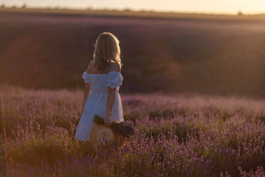 Woman lavender field sunset holding straw hat romantic walk golden hour atmosphere