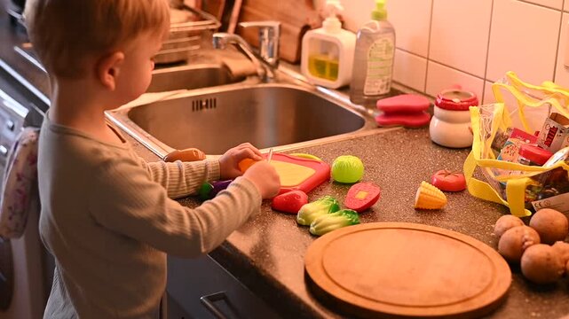 Cute toddler playing with toy vegetables in cozy home kitchen. Child learning through pretend cooking and educational play at home