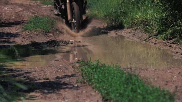 Slow motion close up of enduro motorcycle riding through mud puddle on dirt road outdoor
