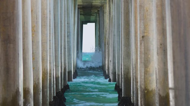 long lens shot of waves breaking on the pylons of the pier at the beach